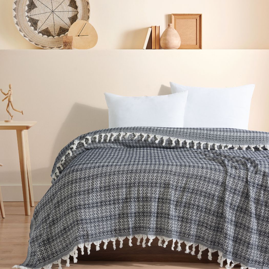 Couvre-lit 100% en coton, de dimensions 230 x 200 cm, avec un motif géométrique noir et blanc. Le tissu tissé est orné de franges nouées sur les bords, ajoutant une touche élégante et artisanale. Il apporte une ambiance chaleureuse et sophistiquée à la chambre.
