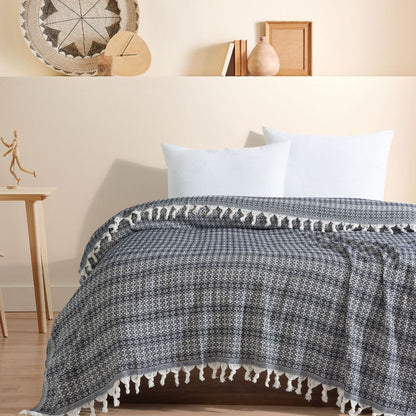 Couvre-lit 100% en coton, de dimensions 230 x 200 cm, avec un motif géométrique noir et blanc. Le tissu tissé est orné de franges nouées sur les bords, ajoutant une touche élégante et artisanale. Il apporte une ambiance chaleureuse et sophistiquée à la chambre.