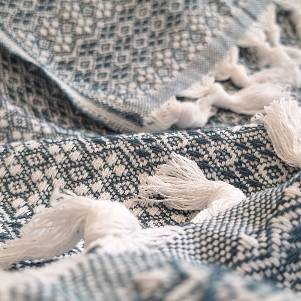 Couvre-lit en 100% coton, de dimensions 230 x 200 cm, avec un motif géométrique en vert émeraude et blanc. Le tissu présente une texture tissée détaillée et est orné de franges nouées, apportant une touche élégante et artisanale