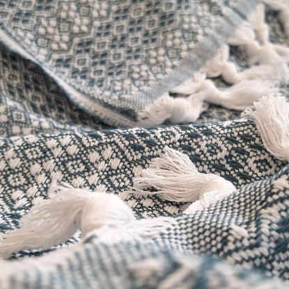 Couvre-lit en 100% coton, de dimensions 230 x 200 cm, avec un motif géométrique en vert émeraude et blanc. Le tissu présente une texture tissée détaillée et est orné de franges nouées, apportant une touche élégante et artisanale